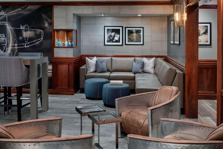 Upscale lounge with gray sectional sofa, copper aircraft-inspired chairs, and aviation-themed wall art and decor.