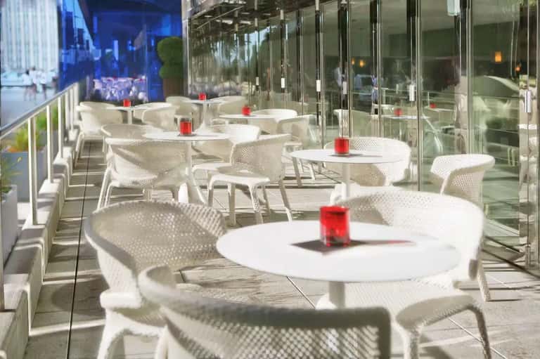 Rooftop dining terrace with white mesh chairs, round tables, and red candles overlooking city skyline.