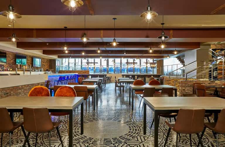 Modern dining hall with exposed brick, wooden beams, pendant lighting, and colorful accent chairs.