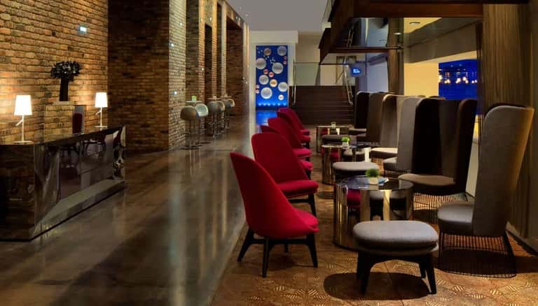 Luxury lounge with exposed brick walls, red velvet chairs, modern furnishings, and contemporary artwork.