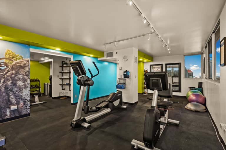 Fitness center with lime-green accent walls, exercise bikes, treadmill, dumbbells, and floor-to-ceiling windows.