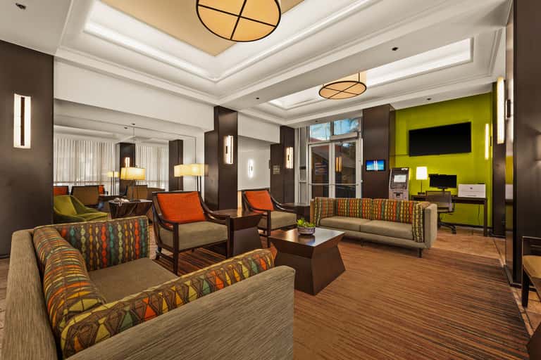 Modern hotel suite with orange and lime green accents, comfortable seating, and flat-screen TV