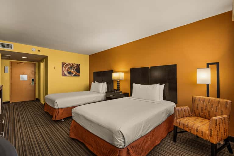 Hotel guest room with two queen beds, orange walls, and modern furnishings