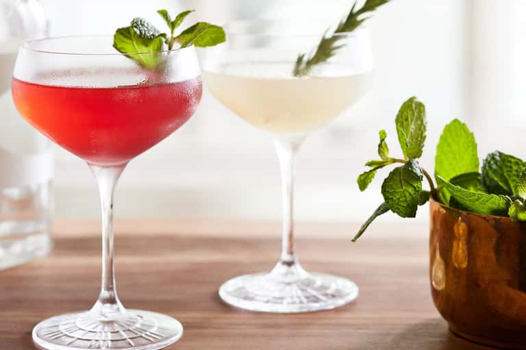 Two colorful cocktails with mint garnish and fresh herbs on a wooden surface