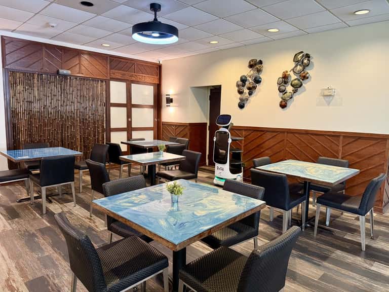 Modern hotel lounge with blue-topped tables, black chairs, wooden wall paneling, and decorative metal wall art