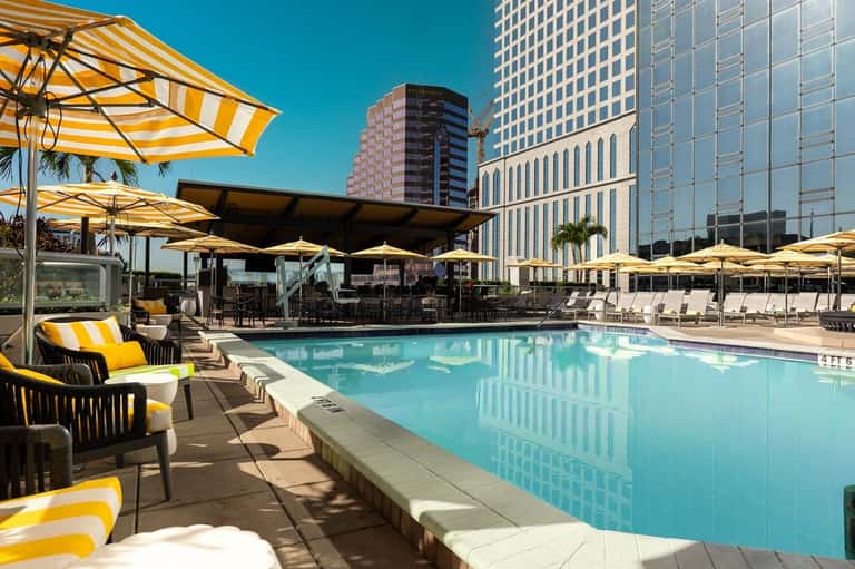 Resort pool with turquoise water, yellow and white striped umbrellas, lounge chairs, and downtown skyline views
