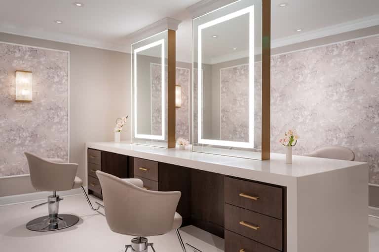 Professional salon vanity with dual LED-lit mirrors, dark wood cabinetry, white countertop, and upholstered chairs