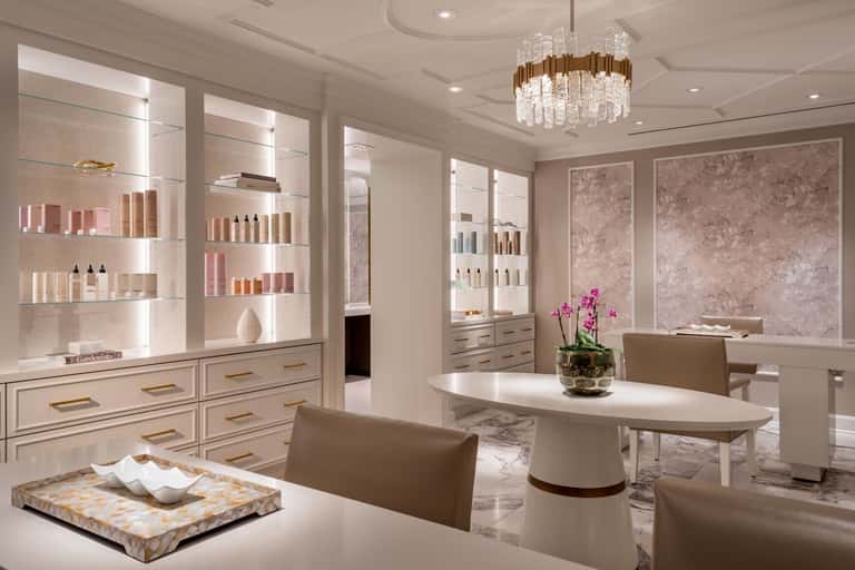 Luxury spa retail space with illuminated product displays, glass shelving, crystal chandelier, and marble flooring