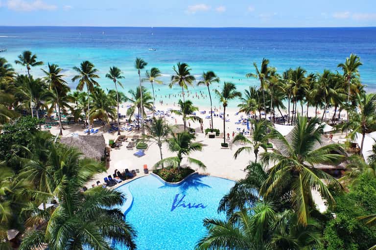 Tropical beach resort with curved pool, palm trees, and ocean view with sunbathers
