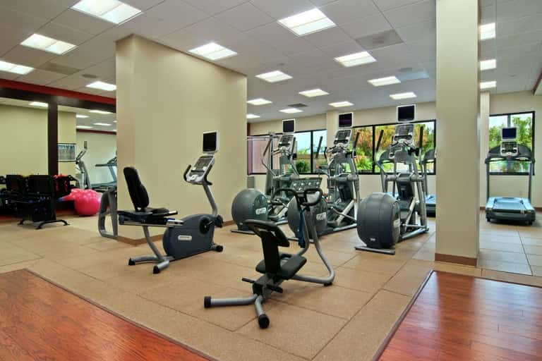 Fitness center with cardio equipment, exercise bikes, mirrors, and large windows with natural light