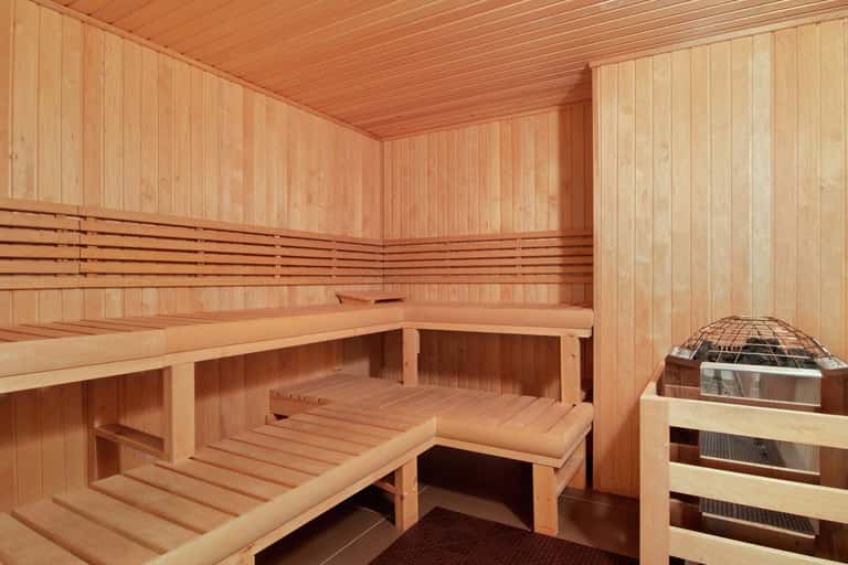 Wooden sauna interior with benches, vertical paneling, and traditional heater with metal cage