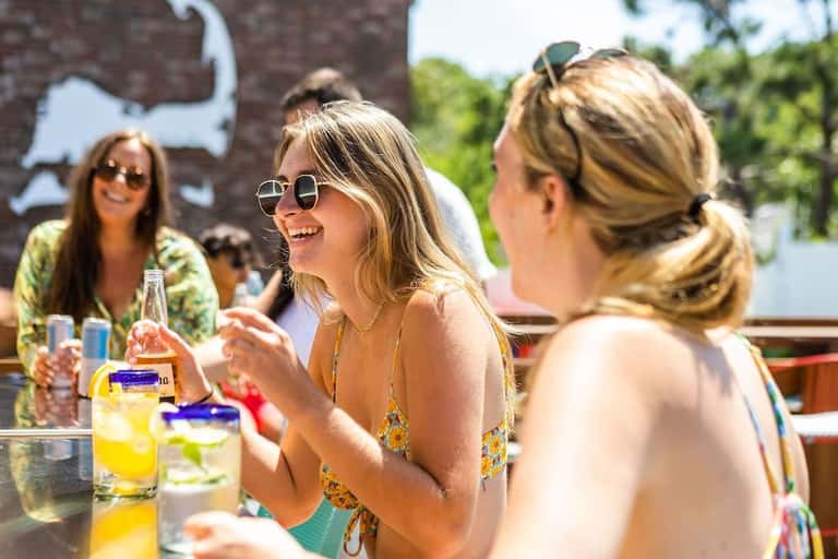 Women enjoying drinks and conversation at an outdoor poolside bar during daytime