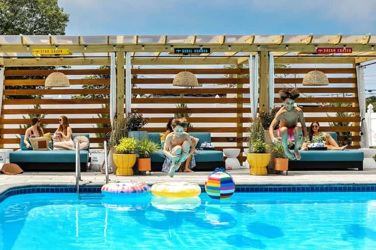 Resort pool with lounge seating, colorful striped pergola, and guests enjoying water activities