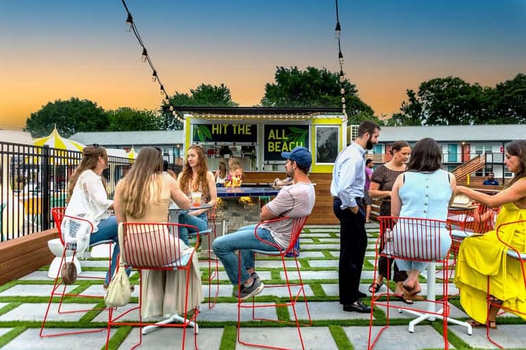 Rooftop gathering space at dusk with food truck, guests mingling, and string lights overhead