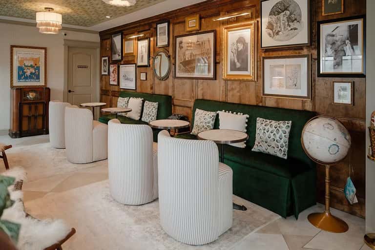Vintage-inspired lounge with wood paneling, green velvet benches, striped armchairs, and eclectic framed artwork