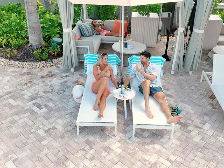 Couple relaxing on striped lounge chairs under white canopy tent with coastal greenery backdrop