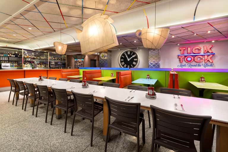 Modern dining space with colorful booths, pendant lighting, and Tick Tock neon sign on wall