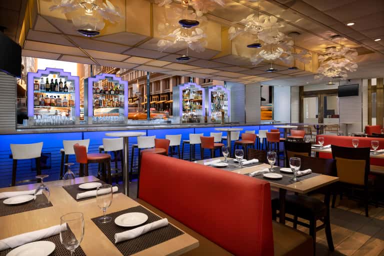 Contemporary restaurant interior with blue bar, red seating, decorative ceiling fixtures, and place settings