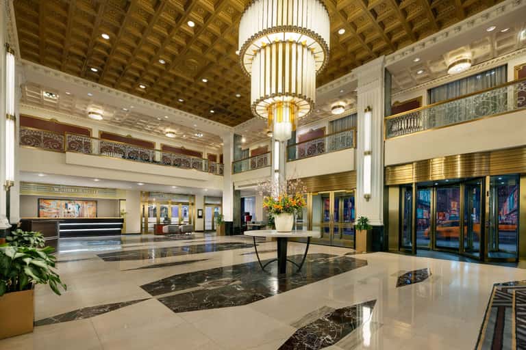 Grand hotel lobby featuring ornate coffered ceiling, central chandelier, marble floors, and elegant archways