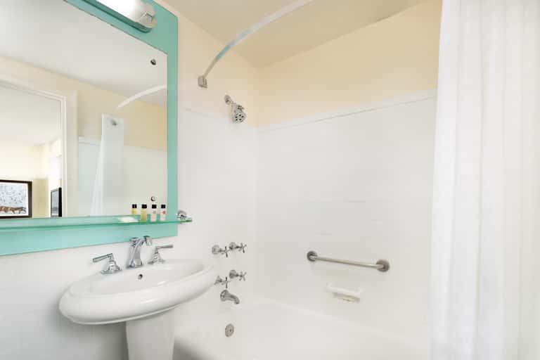 Modern bathroom with turquoise-framed mirror, white pedestal sink, and walk-in shower with grab bars