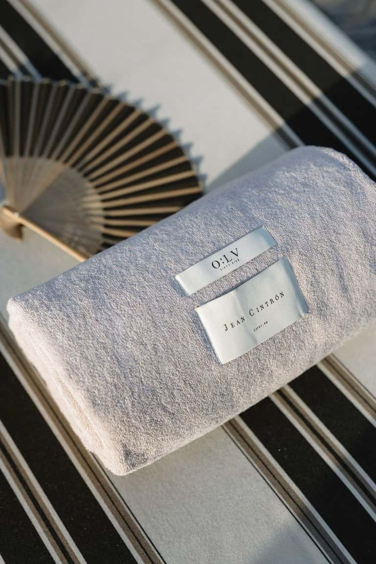 Folded gray towel with OILY and Jean Cintron labels on striped lounge chair