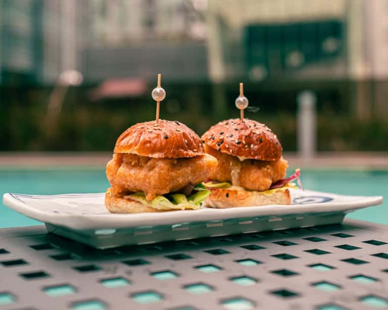 Two gourmet sliders with sesame seed buns on a white plate by the pool