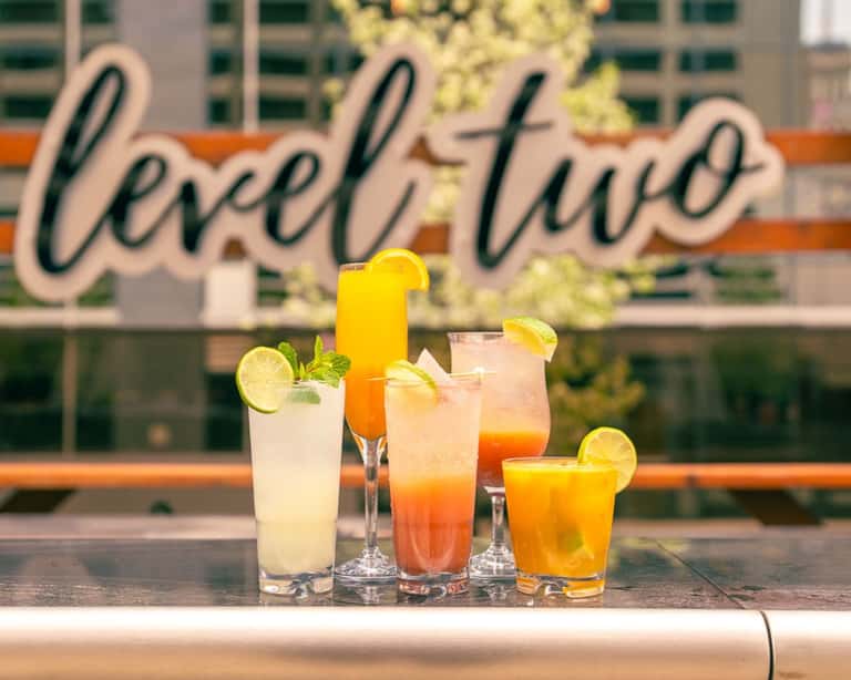 Assorted colorful cocktails with citrus garnishes in front of 'Level Two' signage
