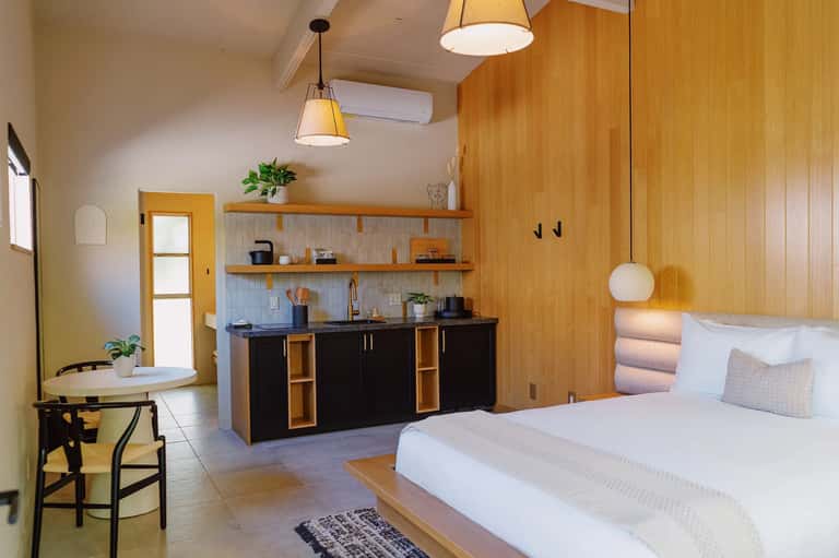 Modern studio room with wooden accents, kitchenette, bed, and pendant lighting