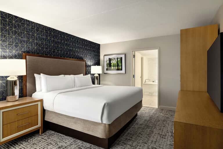 Hotel bedroom with queen bed, wood nightstands, geometric accent wall, and ensuite bathroom entrance