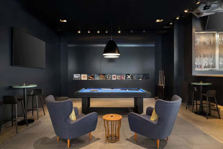 Sophisticated recreation room featuring pool table, blue armchairs, pendant lighting, and bar area