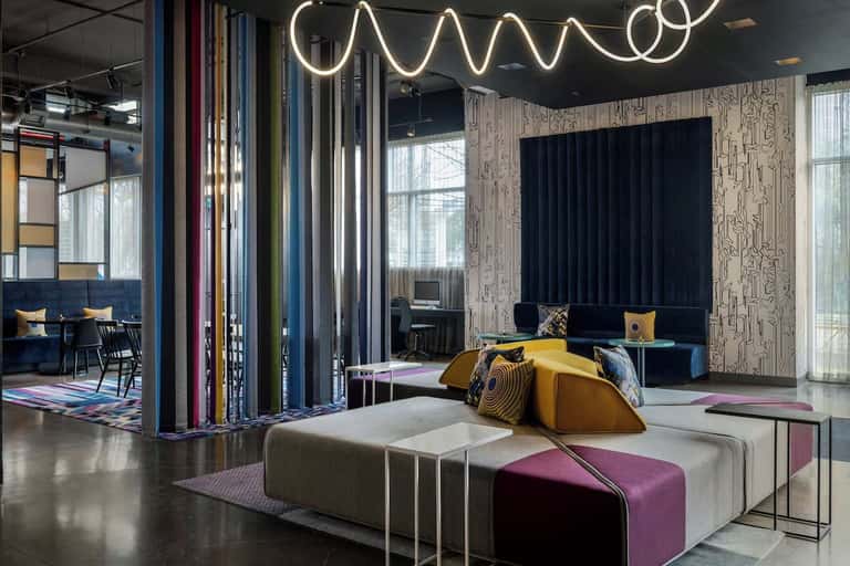 Modern lounge with modular seating in yellow and purple, neon wavy light fixture, and contemporary decor