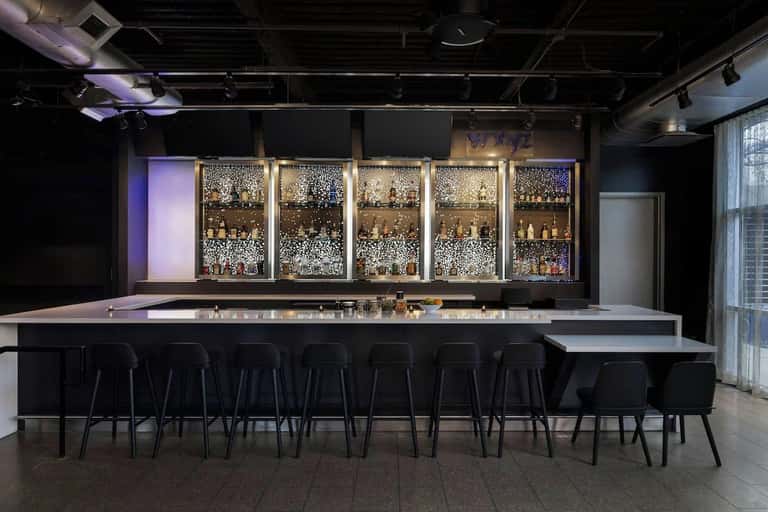 Sleek bar counter with illuminated shelving displaying bottles and dark modern design elements
