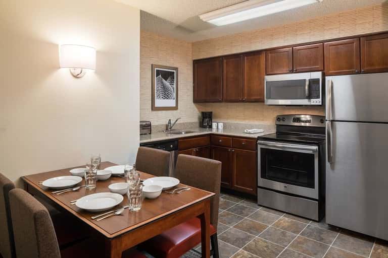 Suite kitchenette with wood dining table, stainless steel appliances, brown cabinetry, and tiled flooring