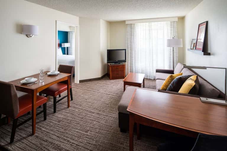 Extended stay suite with separate living and sleeping areas, wood furnishings, and access to bedroom