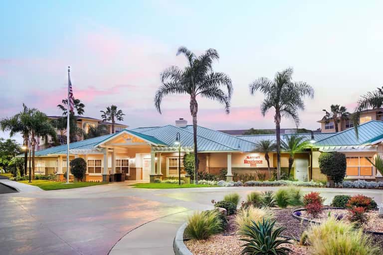 Resort exterior at dusk with palm trees, blue metal roof, manicured landscaping, and warm lighting