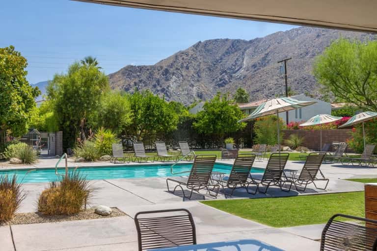 Resort pool area with loungers, umbrellas, mountains in background, and lush landscaping
