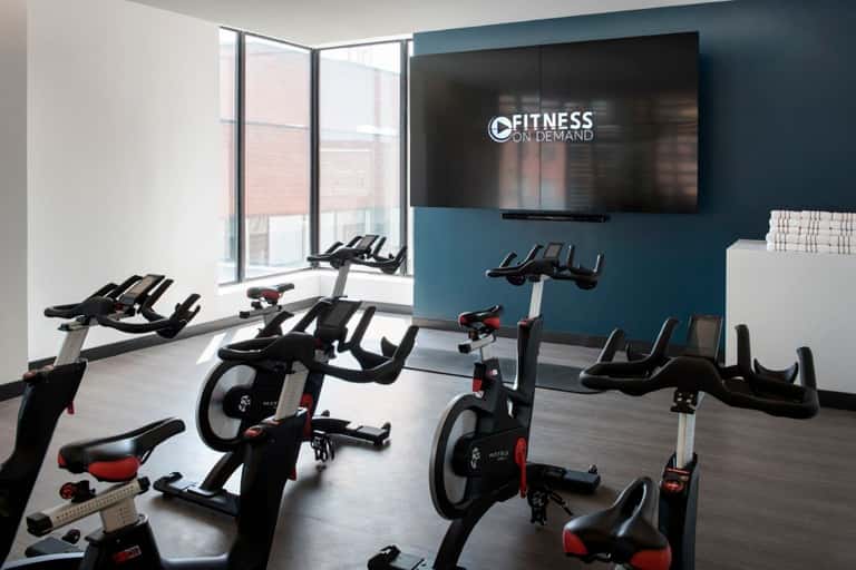 Indoor cycling studio with stationary bikes, large screen displaying Fitness On Demand, and blue accent walls