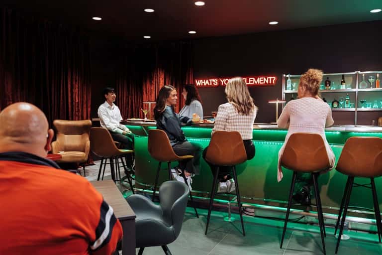 Social gathering at a trendy bar lounge with neon green signage and leather seating