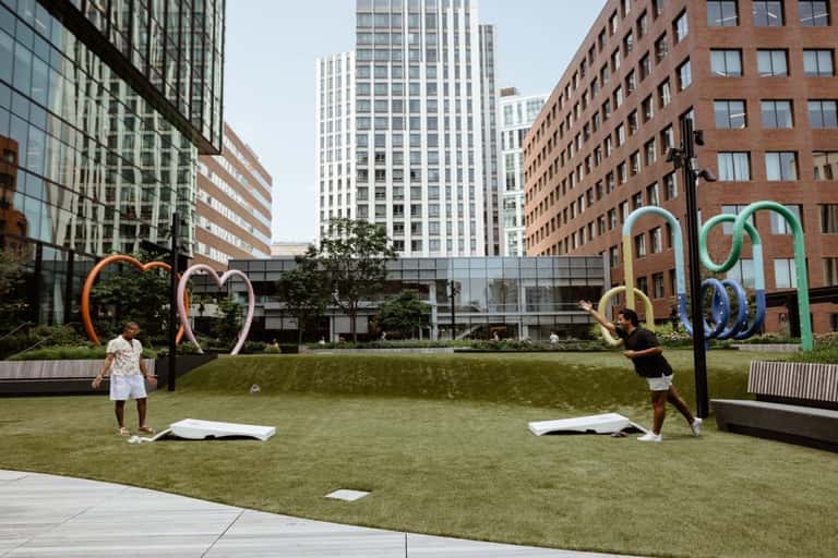 Outdoor fitness space in urban courtyard with colorful sculptural rings and people exercising on grass