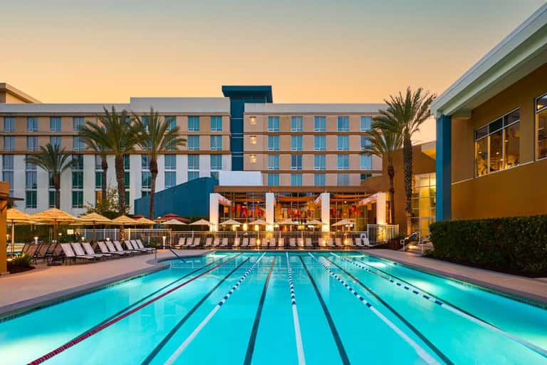 Olympic-length lap pool with lane dividers at dusk, hotel buildings and palm trees in background