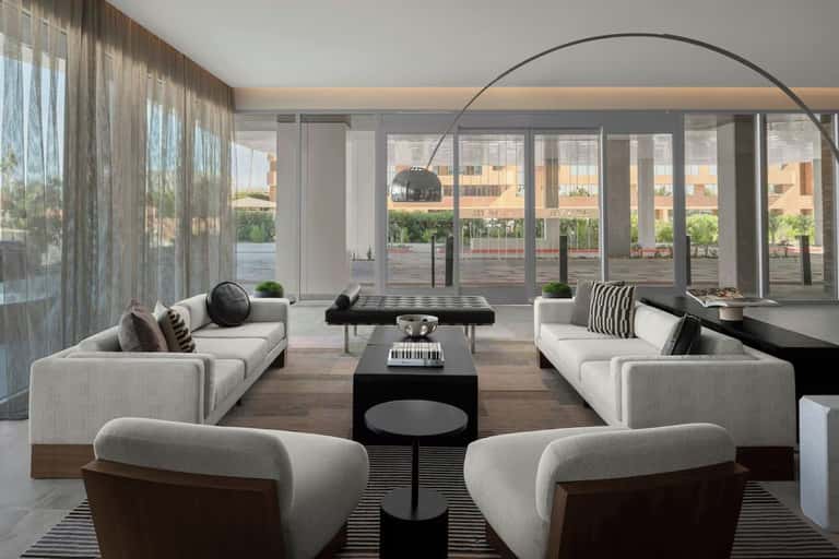 Modern living room with white sectional seating, floor-to-ceiling windows, and city views
