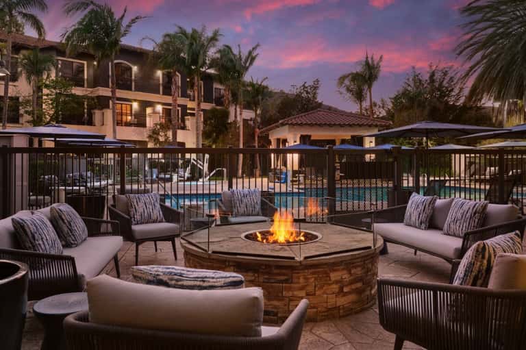 Evening fire pit lounge with gray seating, striped pillows, pool view, and dramatic purple sunset sky