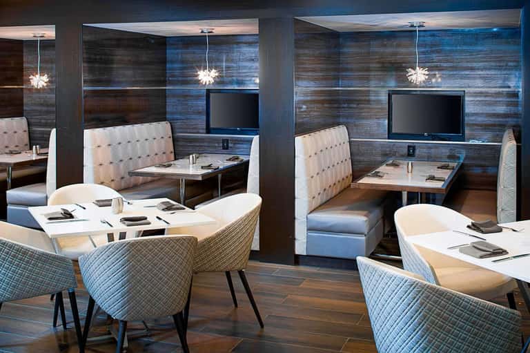 Modern upscale restaurant dining area with blue accent walls, white pendant lights, booths with patterned seating, and flat-screen TVs