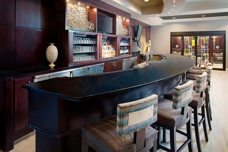 Elegant curved bar with dark wood cabinetry, bottle displays, illuminated shelving, bar stools, and modern pendant lighting