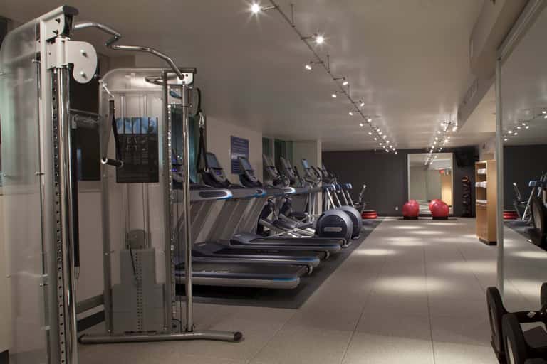 Modern fitness center with multiple treadmills, cardio equipment, mirrored walls, track lighting, and exercise machines