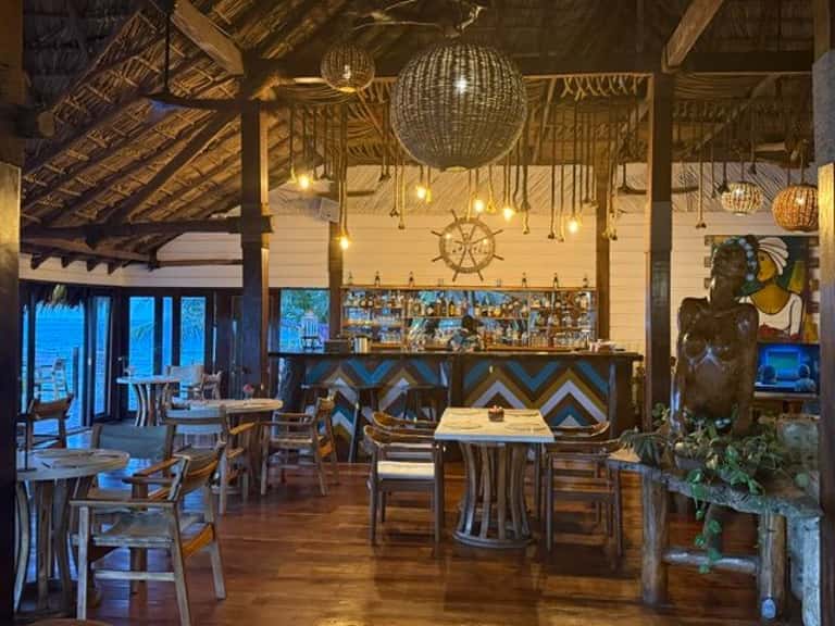 Upscale restaurant interior with wooden beams, hanging globe lights, bar, and ocean views