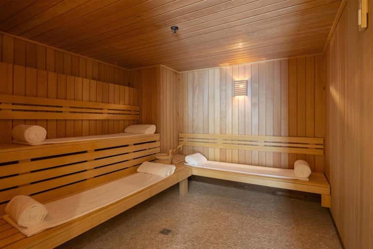 Wooden sauna interior with tiered benches, rolled towels, and stone floor
