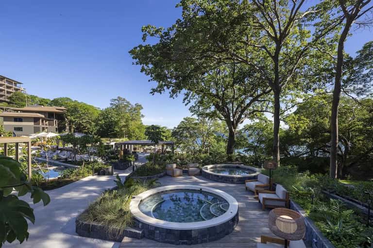 Spa area with circular hot tubs on wooden deck surrounded by large trees and tropical garden