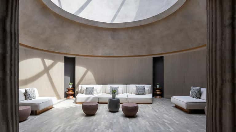 Minimalist spa relaxation room with circular skylight, curved walls, and modern white seating