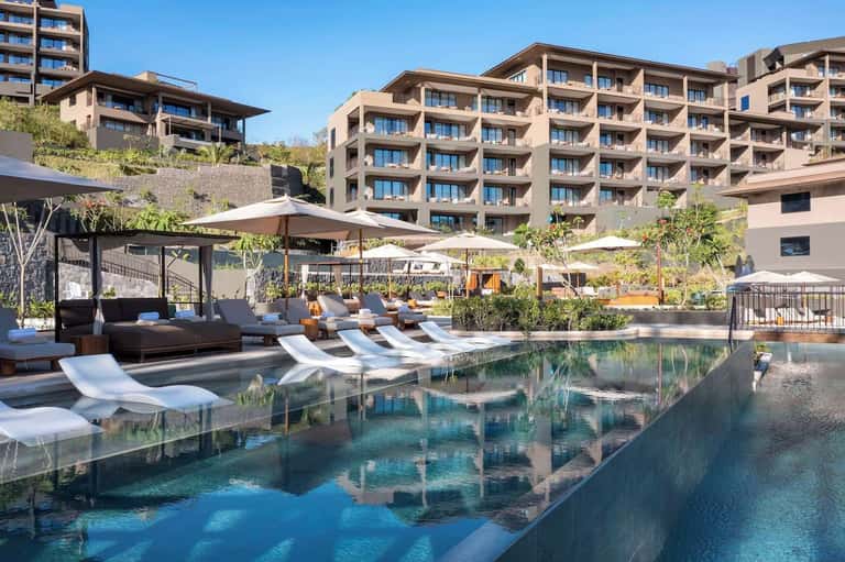 Contemporary resort pool deck with loungers, canopy beds, shade structures, and modern architecture